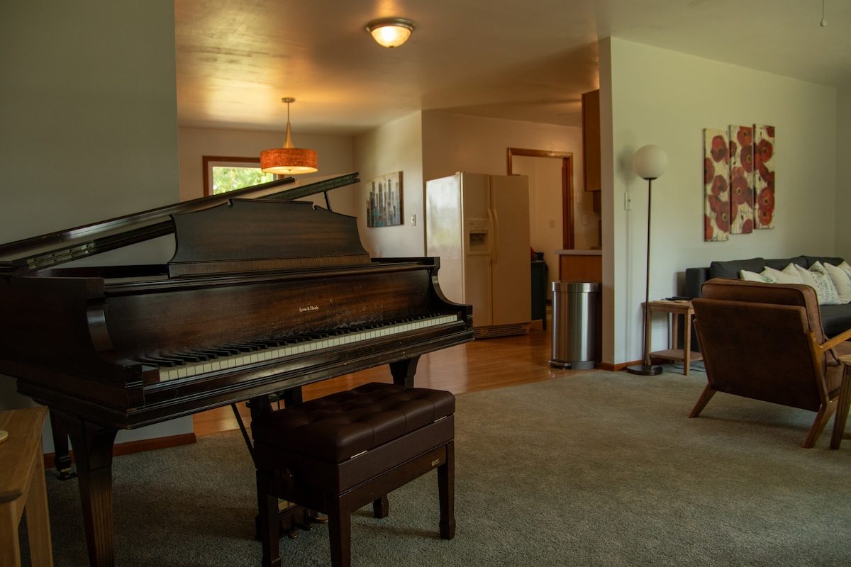 The living room, with the baby grand piano and the kitchen beyond